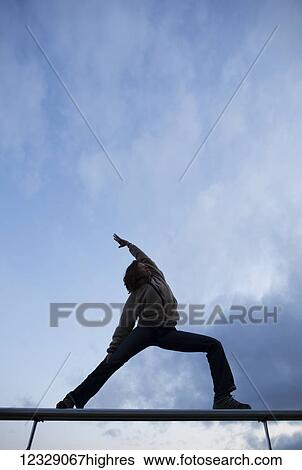 Stock Photograph - Low angle view of a woman doing a yoga pose on bleachers with a cloudy sky; Alaska, United States of America. Fotosearch