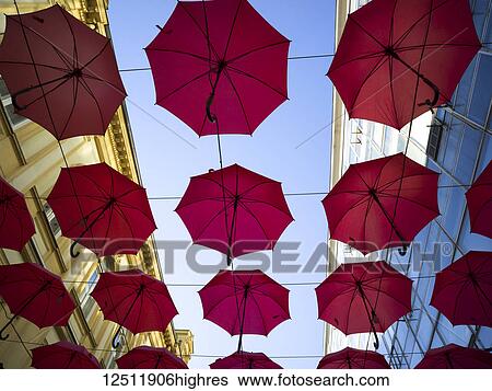 Stock Photograph - Low angle view of red umbrellas suspended overhead with buildings on either side and a blue sky; Belgrade, Vojvodina, Serbia. Fotosearch