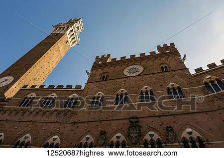 Stock Photograph - Low angle view of stone wall of town hall with Mangia tower and blue sky; Siena, Tuscany, Italy. Fotosearch