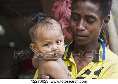 Stock Image - Man holding a baby at the market; Dili, East Timor. Fotosearch