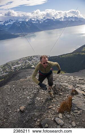 Stock Image - Man tops out on the summit ridge of Mount Marathon trail, above Seward, Southcentral Alaska, Summer. Fotosearch