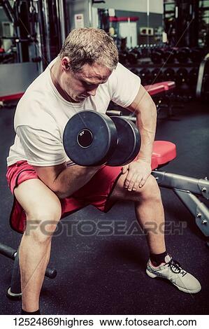 Stock Photograph - Middle-aged man working out and doing bicep curls at a fitness facility; Spruce Grove, Alberta, Canada. Fotosearch