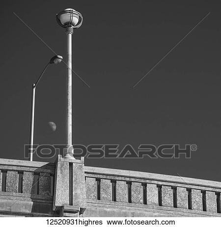 Stock Photograph - Moon viewed between street light and bridge lamp post; Winnipeg, Manitoba, Canada. Fotosearch