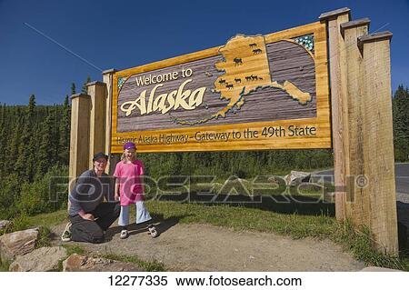 Stock Photography - Mother and daughter pose beneath the Welcome to Alaska highway sign, Alaska Canada Boarder, Alaska, USA, Summer. Fotosearch