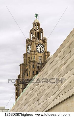 Stock Photograph - Old Liverpool building with clock tower behind the modern wall of the museum; Liverpool, England. Fotosearch