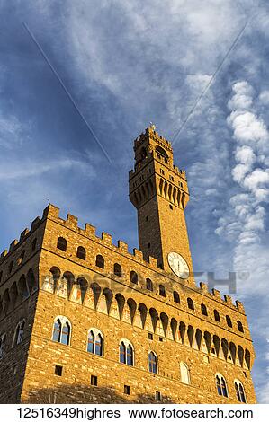 Stock Photograph - Old stone castle and tower with dramatic clouds and blue sky glowing orange at sunset; Florence, Tuscany, Italy. Fotosearch