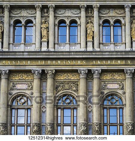 Stock Photograph - Ornate facade of a building with pillars and statues beside windows with reflection of the blue sky; Budapest, Budapest, Hungary. Fotosearch