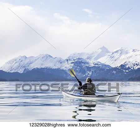 Stock Photograph - Paddling in a canoe on tranquil water with a view of the snow capped Kenai Mountains, Kachemak Bay State Park; Alaska, United States of America. Fotosearch