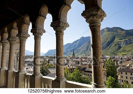 Stock Photograph - Palace stone columns frames an alpine village in the background with mountains and blue sky; Trento, Trento, Italy. Fotosearch