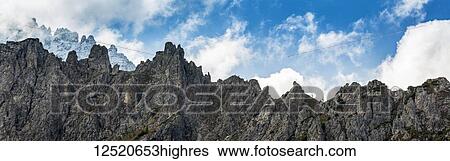 Stock Photograph - Panorama of rugged mountain peaks with blue sky and cloud; Sesto, Bolzano, Italy. Fotosearch