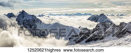 Panorama of snow-covered mountain peaks with cloud cover exposing peaks; Grainau, Bavaria, Germany View Large Photo Image Stock Photograph - Panorama of snow-covered mountain peaks with cloud cover exposing peaks; Grainau, Bavaria, Germany. Fotosearch