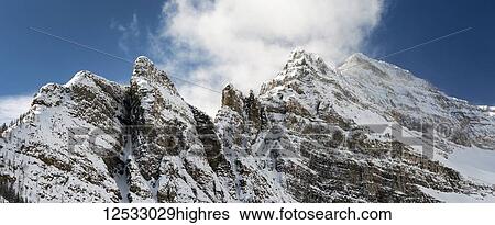 Stock Photograph - Panorama of snow-covered rugged mountain peaks with blue sky and clouds, Banff National Park; Lake Louise, Alberta, Canada. Fotosearch