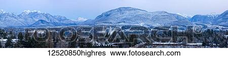 Stock Photograph - Panoramic of snowy Cascade mountain range with the town of Surrey in the foreground, lower mainland; Surrey, British Columbia, Canada. Fotosearch
