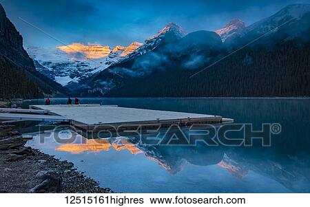Stock Photograph - Peaks of the Rocky Mountains illuminated by sunlight and reflected in Lake Louise; Lake Louise, Alberta, Canada. Fotosearch