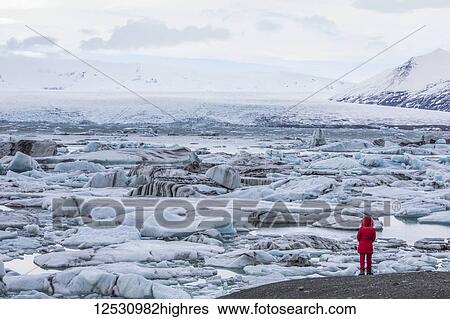 Stock Photograph - Person standing looking at the ice and icebergs at Jokulsarlon, South coast; Iceland. Fotosearch