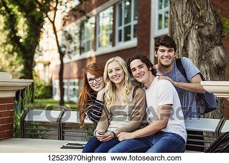 Stock Photograph - Portrait of a group of four friends sitting on a bench on a university campus; Edmonton, Alberta, Canada. Fotosearch
