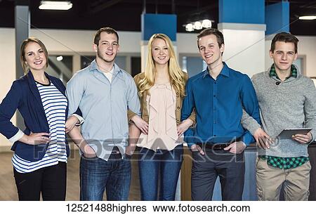 Stock Photograph - Portrait of a group of young millennial professionals standing together arm in arm in the workplace; Sherwood Park, Alberta, Canada. Fotosearch