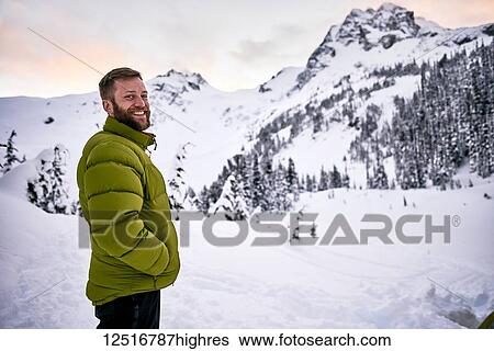 Stock Photograph - Portrait of a man standing in the snow-covered mountains at dusk; British Columbia, Canada. Fotosearch