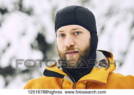 Stock Photograph - Portrait of a man with a frosty beard wearing a head covering against a snowy background; British Columbia, Canada. Fotosearch
