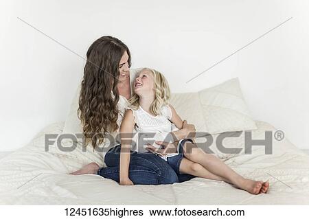 Stock Photograph - Portrait of a mother and young daughter sitting on a bed spending time together; Sorrento, British Columbia, Canada. Fotosearch