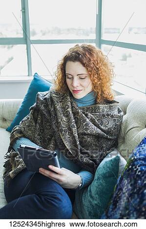Stock Photograph - Portrait of a woman sitting with a laptop by a window; Surrey, British Columbia, Canada. Fotosearch