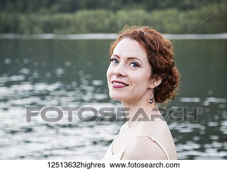Stock Photograph - Portrait of a woman with red hair and a lake in the background; British Columbia, Canada. Fotosearch