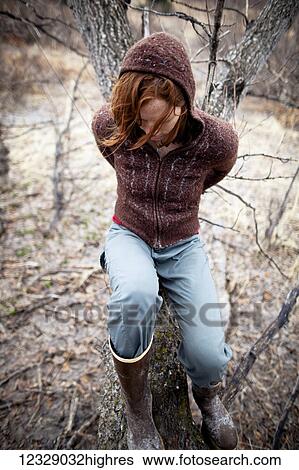 Stock Photograph - Portrait of a woman with red hair leaning on a cottonwood tree and looking contemplative; Homer, Alaska, United States of America. Fotosearch