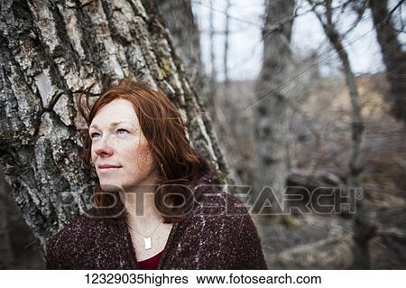 Portrait of a woman with red hair against a tree and looking contemplative; Homer, Alaska, United States of America View Large Photo Image Stock Photograph - Portrait of a woman with red hair against a tree and looking contemplative; Homer, Alaska, United States of America. Fotosearch