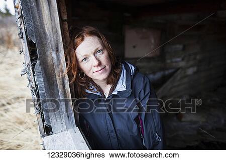 Portrait of a woman with red hair leaning against a wooden wall and looking up at the camera; Alaska, United States of America View Large Photo Image Stock Photograph - Portrait of a woman with red hair leaning against a wooden wall and looking up at the camera; Alaska, United States of America. Fotosearch