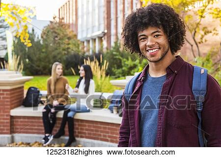 Stock Photograph - Portrait of a young African American male university student posing with his friends talking together in the background on the university campus; Edmonton, Alberta, Canada. Fotosearch