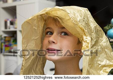 Stock Photograph - Portrait of a young boy with a piece of wrapping paper on his head making a silly face; Langley, British Columbia, Canada. Fotosearch