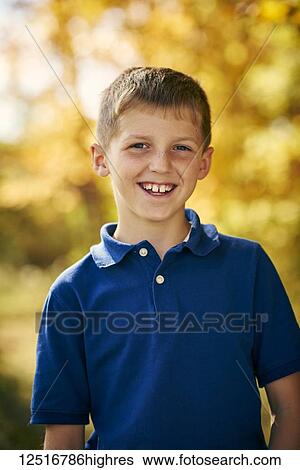 Stock Photograph - Portrait of a young boy with a toothy smile and autumn coloured foliage in the background; Ontario, Canada. Fotosearch