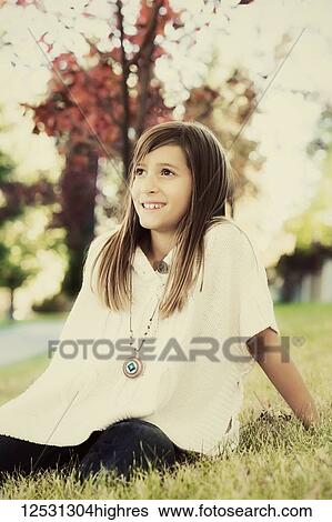 Stock Photograph - Portrait of a young girl sitting on the grass in a park in autumn; Edmonton, Alberta, Canada. Fotosearch