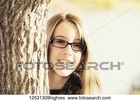 Portrait of a young girl with eyeglasses peering out from behind a tree in autumn; Edmonton, Alberta, Canada View Large Photo Image Stock Photograph - Portrait of a young girl with eyeglasses peering out from behind a tree in autumn; Edmonton, Alberta, Canada. Fotosearch