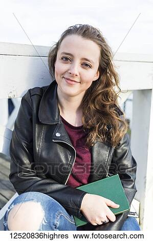 Stock Photograph - Portrait of a young woman holding a book; New Westminster, British Columbia, Canada. Fotosearch