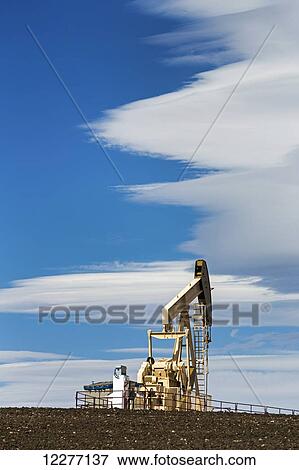 Pumpjack on a hill with dramatic clouds in the blue sky; Alberta, Canada View Large Photo Image Stock Photo - Pumpjack on a hill with dramatic clouds in the blue sky; Alberta, Canada. Fotosearch