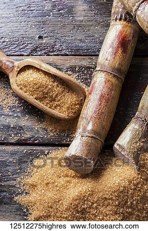 Stock Photograph - Raw sugar cane on a wooden surface and in a wooden scoop. Fotosearch
