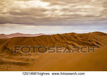 Stock Photograph - Red sand dunes in the Namib desert under a cloudy sky, Namib-Naukluft National Park; Sossusvlei, Hardap Region, Namibia. Fotosearch