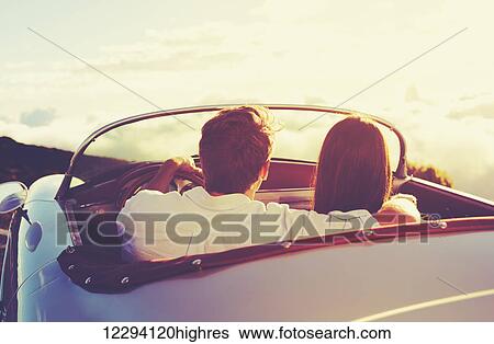 Stock Photograph - Romantic Young Attractive Couple Watching The Sunset In Classic Vintage Sports Car. Fotosearch