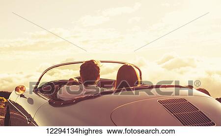 Stock Photograph - Romantic Young Attractive Couple Watching The Sunset In Classic Vintage Sports Car. Fotosearch