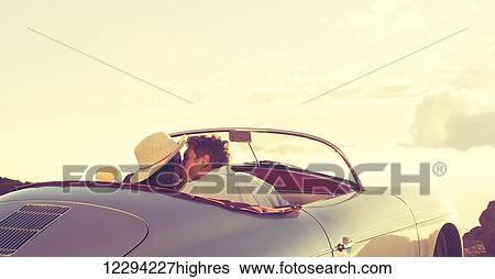 Stock Photograph - Romantic Young Attractive Couple Watching The Sunset And Kissing In Classic Vintage Sports Car. Fotosearch