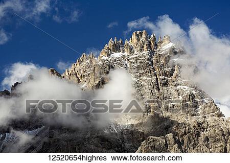 Rugged mountain peak appearing out of clouds with blue sky; Sesto, Bolzano, Italy View Large Photo Image Stock Photograph - Rugged mountain peak appearing out of clouds with blue sky; Sesto, Bolzano, Italy. Fotosearch