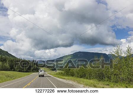 Stock Photograph - RV camper drives down the Alaska Highway, west of Fort Nelson, British Columbia Canada, Summer. Fotosearch