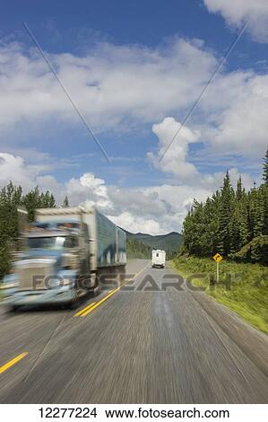 Picture - RV camper drives past a semi truck on the Alaska Highway, west of Fort Nelson, British Columbia Canada, Summer. Fotosearch