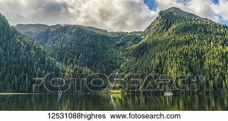 Stock Photograph - Scenic view of the Great Bear Rainforest area with a sailboat on the water; Hartley Bay, British Columbia, Canada. Fotosearch