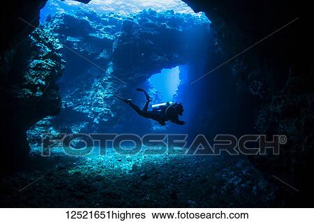 Stock Photograph - Scuba diver swims through lava arches with sun rays, Cathedrals dive site; Lanai City, Lanai, Hawaii, United States of America. Fotosearch