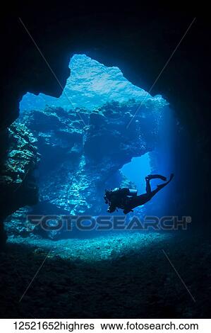 Stock Photograph - Scuba diver swims through lava arches with sun rays, Cathedrals dive site; Lanai City, Lanai, Hawaii, United States of America. Fotosearch