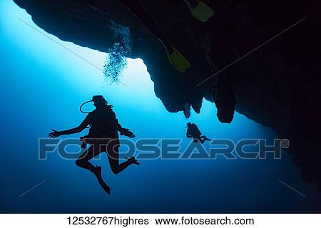 Stock Photograph - Scuba divers in the Great Blue Hole dive site on the Belize Barrier Reef. This site was made famous by Jacques Cousteau, who declared it one of the top five scuba diving sites in the world; Belize. Fotosearch
