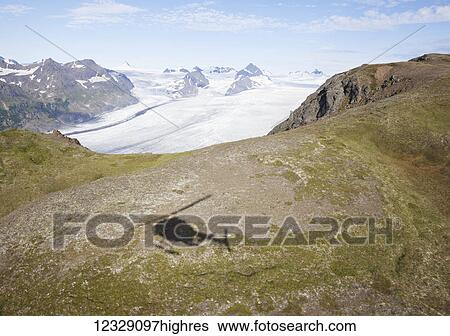 Stock Photograph - Shadow of a helicopter on a plateau overlooking a glacier and Kenai Mountains in Kachemak Bay State Park; Alaska, United States of America. Fotosearch