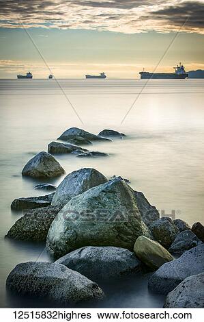 Stock Photograph - Ships out in the Pacific ocean off the coast of Stanley Park with rocks in the foreground; Vancouver, British Columbia, Canada. Fotosearch